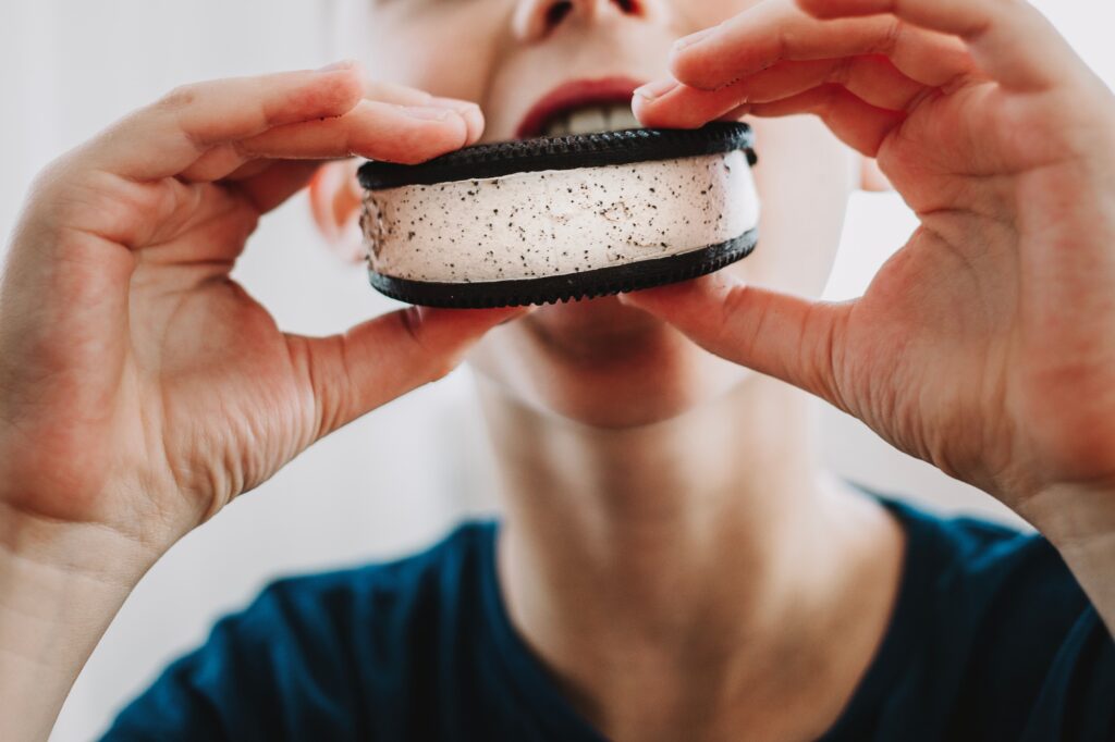 Close up of a little boy biting into an Oreo ice cream sandwich.