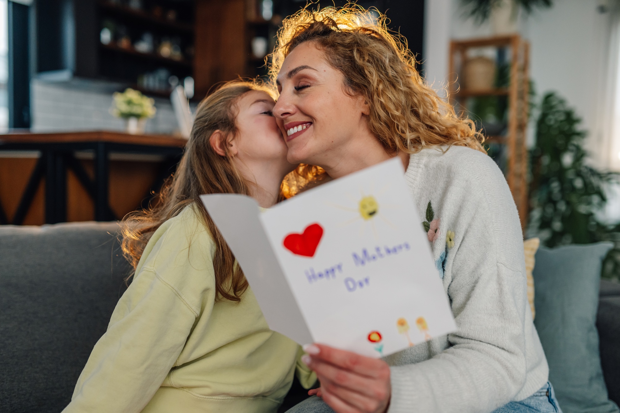 Daughter kissing mother and giving her a handmade greeting card for mother's day